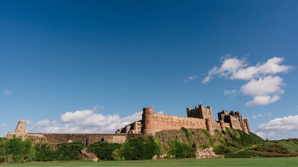 Stone castle on a grassy hilltop under a bright blue sky with scattered clouds.