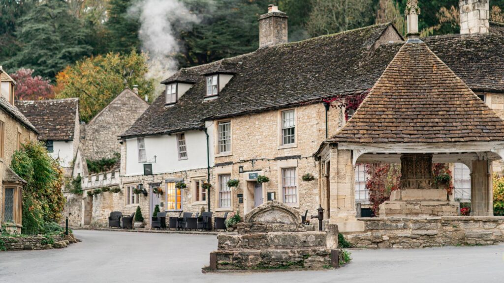 Stone cottage street in a village with outdoor seating and a stone fountain in the foreground.