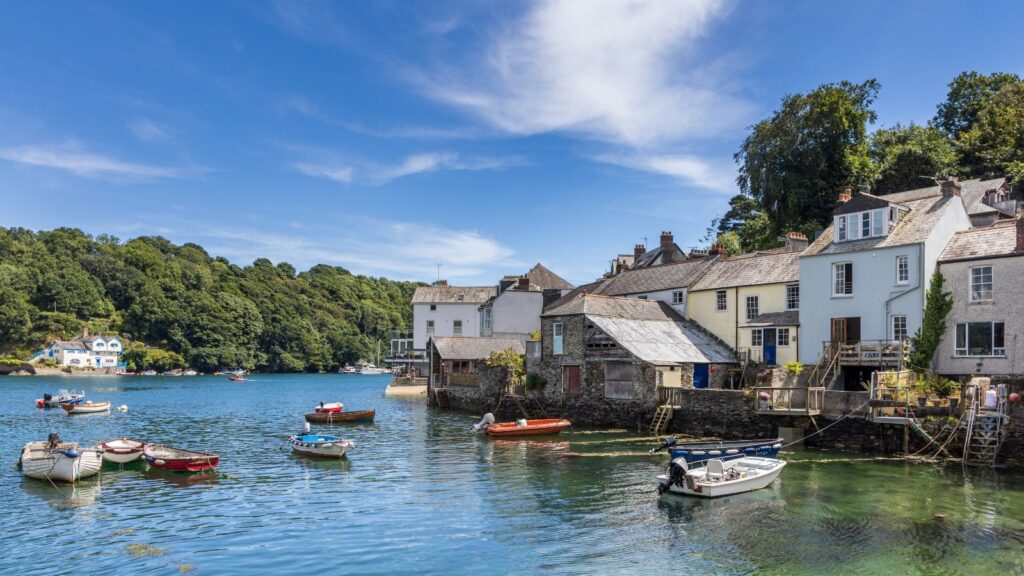 Quaint harbor village with pastel houses along the water and small boats moored in a calm bay under a blue sky. (informative)